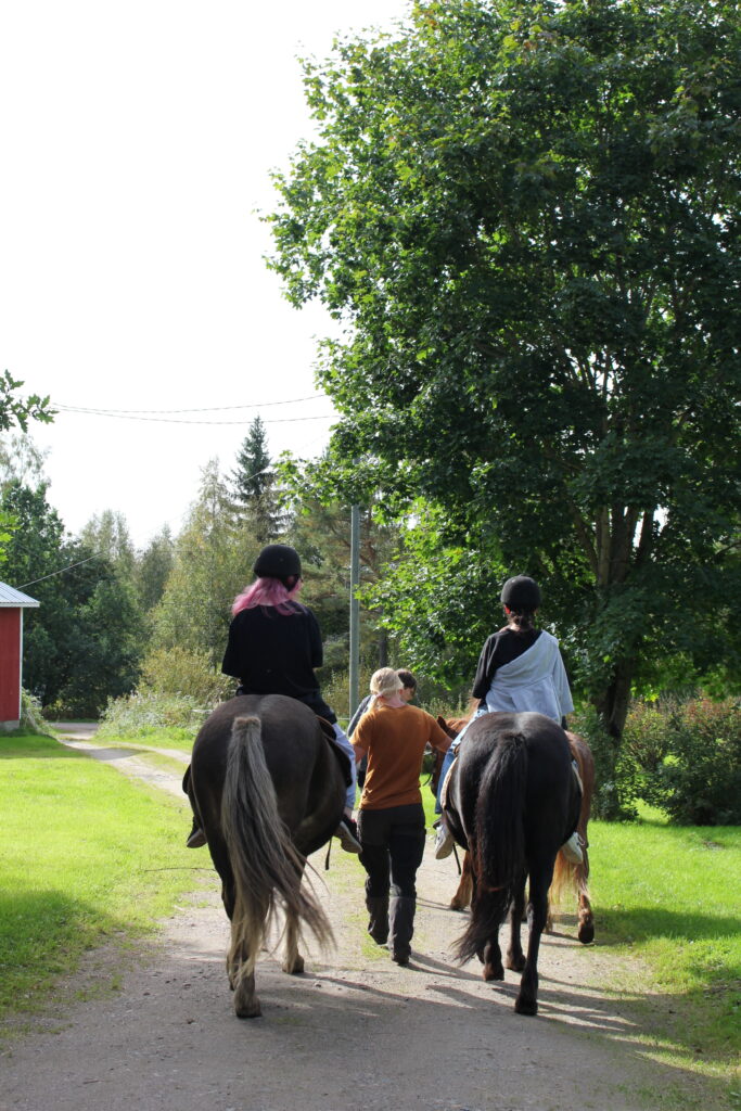 Nainen taluttaa kahta hevosta joiden kyydittä istuu kaksi tyttöä
