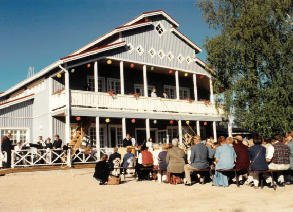 sininen iso rakennus ja pihalla ihmisiä istumassa penkeillä