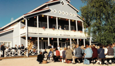 sininen iso rakennus ja pihalla ihmisiä istumassa penkeillä